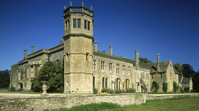 A view looking out from the abbey field towards the south corner of the abbey, with Sharington's Tudor tower at the centre. The sun is shining and the sky is blue.